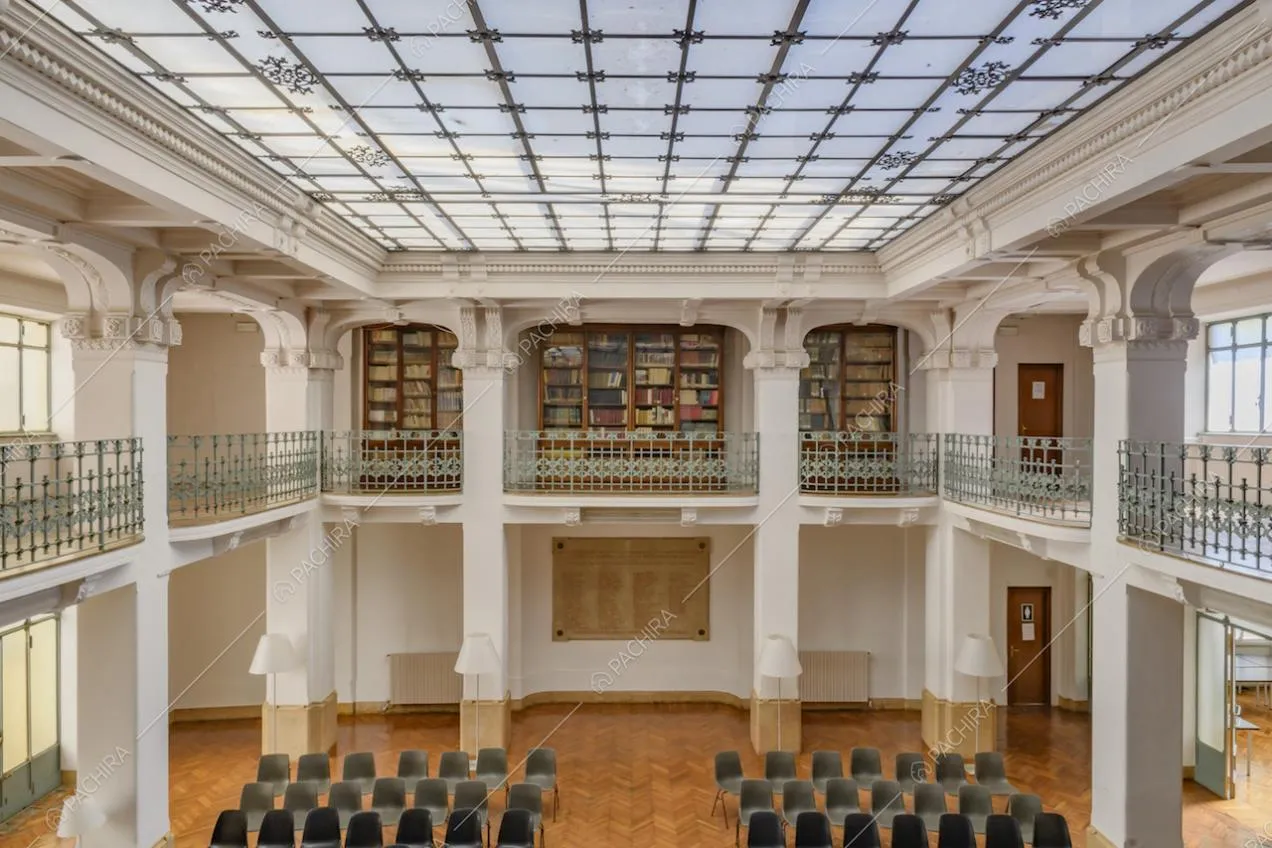 Ampio salone illuminato da lucernario, pareti bianche con colonne e pavimento in parquet a spina di pesce