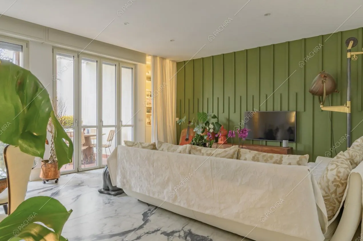 Luminoso salotto con porte-finestre per accedere al balcone con tavolo da pranzo da esterni e parete verde con boiserie