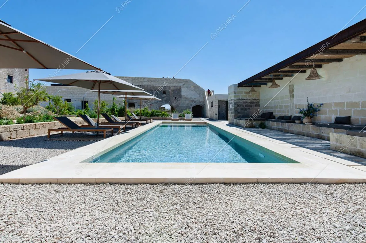 Piscina esterna circondata da ghiaia e muretti in mattoni a vista con cuscini per il relax