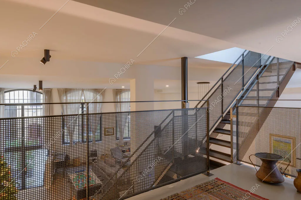 Dal soppalco con balaustra in metallo vista sulle scale e sulla zona living con alto soffitto
