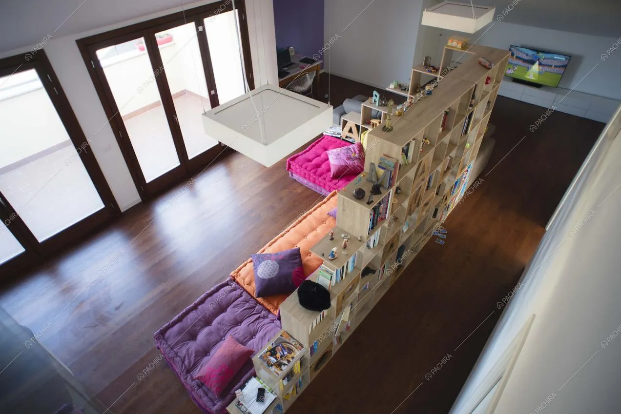 Zona living con divanetti colorati e libreria divisoria, vetrate