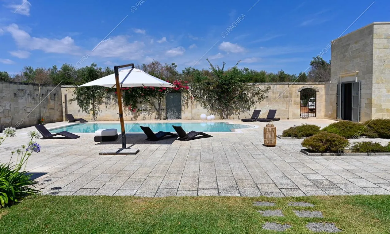 Piscina con ombrellone e lettini nel cortile con pavimentazione in pietra