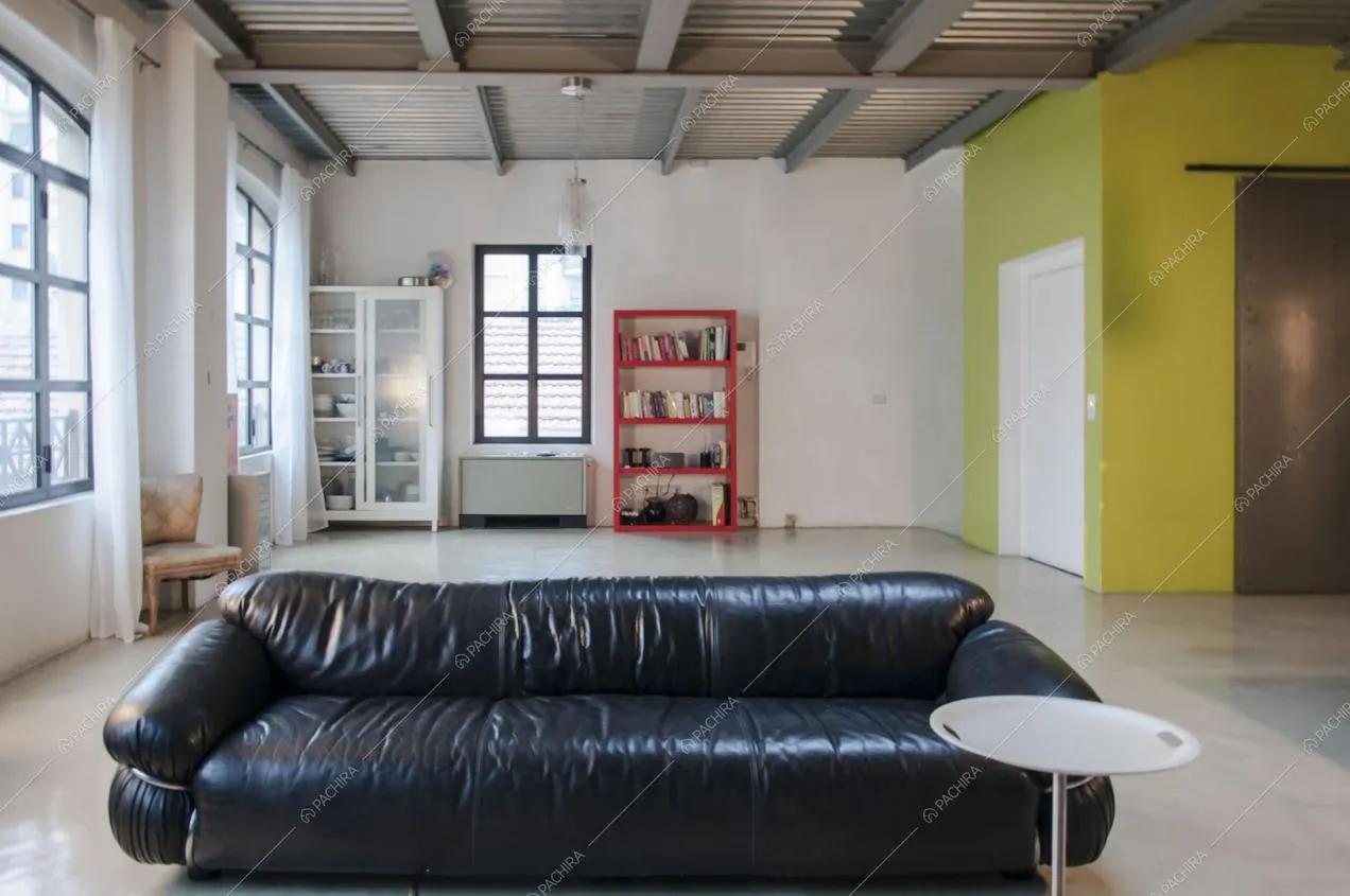 Divano nero in pelle, ampie vetrate e soffitto con travi a vista