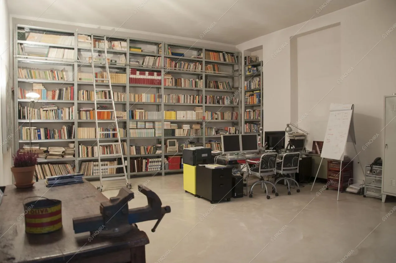 Studio con libreria in metallo a parete, tavolo in legno d'appoggio e scrivania