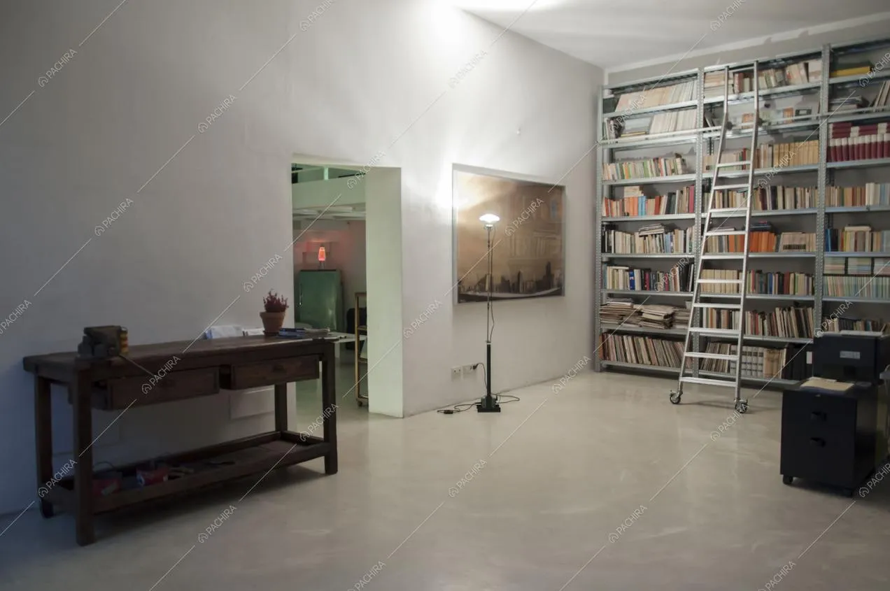 Tavolo in legno d'appoggio, libreria e scorcio sulla cucina dallo studio