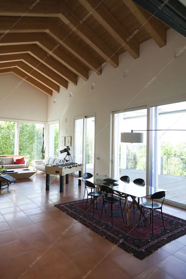 Zona living con ampie vetrate e soffitto alto e con travi in legno a vista
