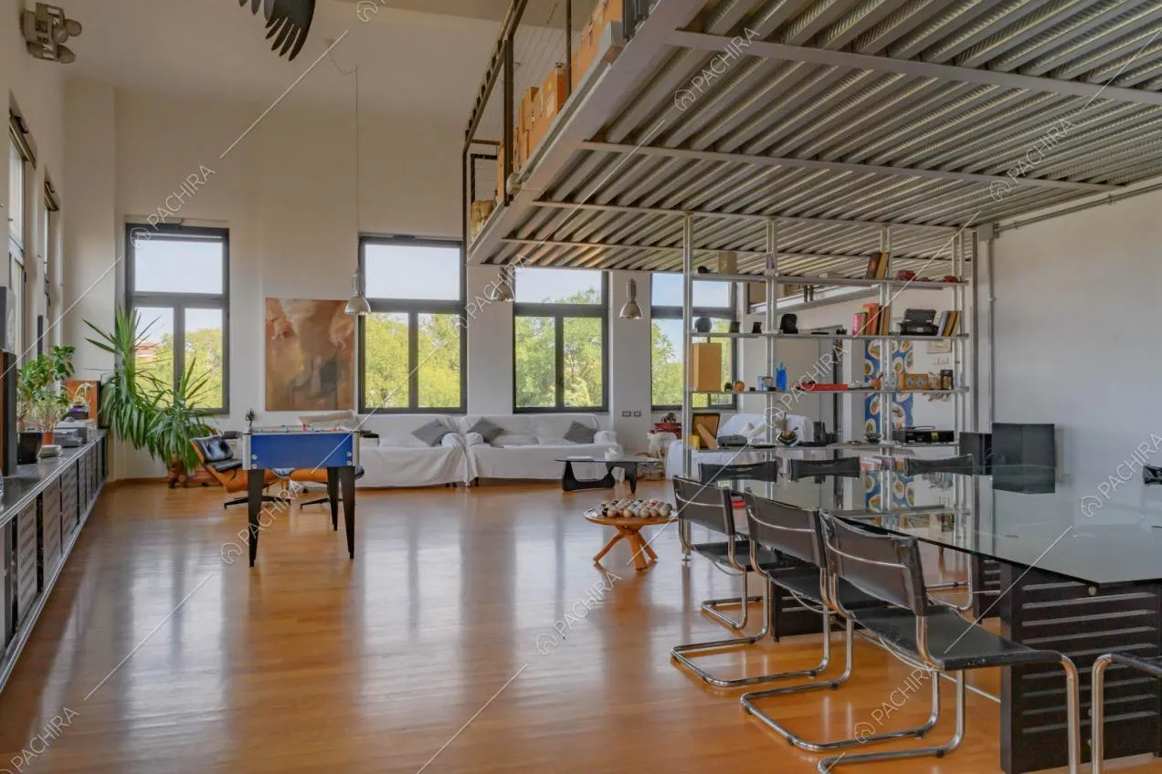 Grande sala con divani bianchi, soppalco in metallo e pavimento in parquet