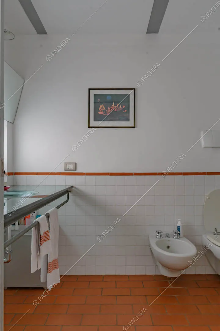 Pareti bianche con mattoni a vista nel bagno con sanitari e pavimento in cotto