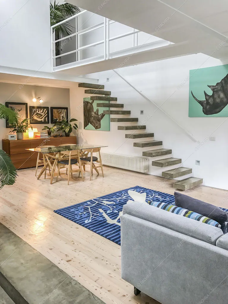 Zona living con divano, scale sospese e tavolo da pranzo