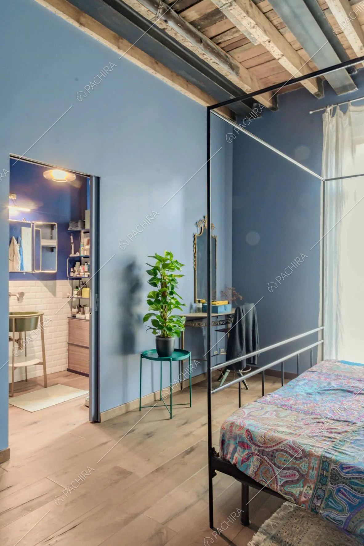 Camera da letto matrimoniale con pareti azzurre, soffitto con travi in legno a vista e bagno privato