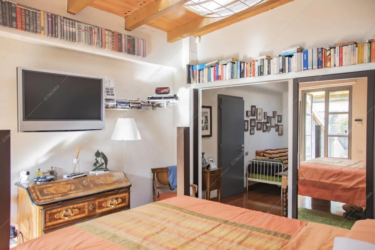 Camera da letto con lucernario sul soffitto con travi in legno a vista e pavimento in parquet