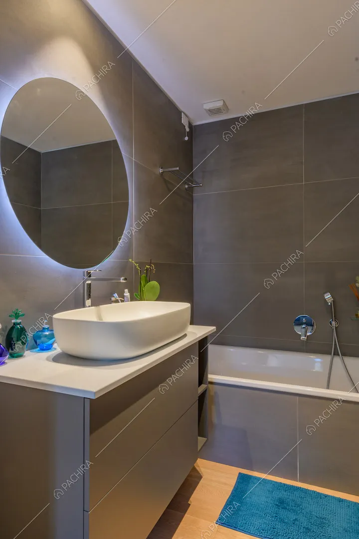 Bagno con pavimento in parquet, pareti grigie, vasca e specchio retro-illuminato