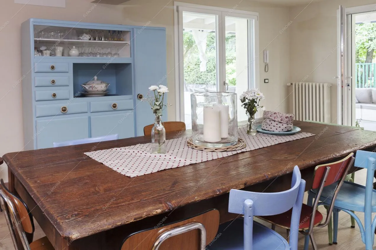 Tavolo da pranzo in legno, credenza azzurra e porte-finestre per accedere alla veranda