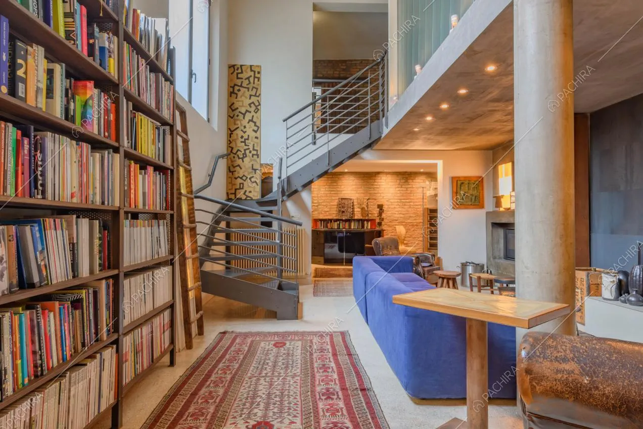 Libreria nella sala con colonna, scala in metallo e divano blu elettrico
