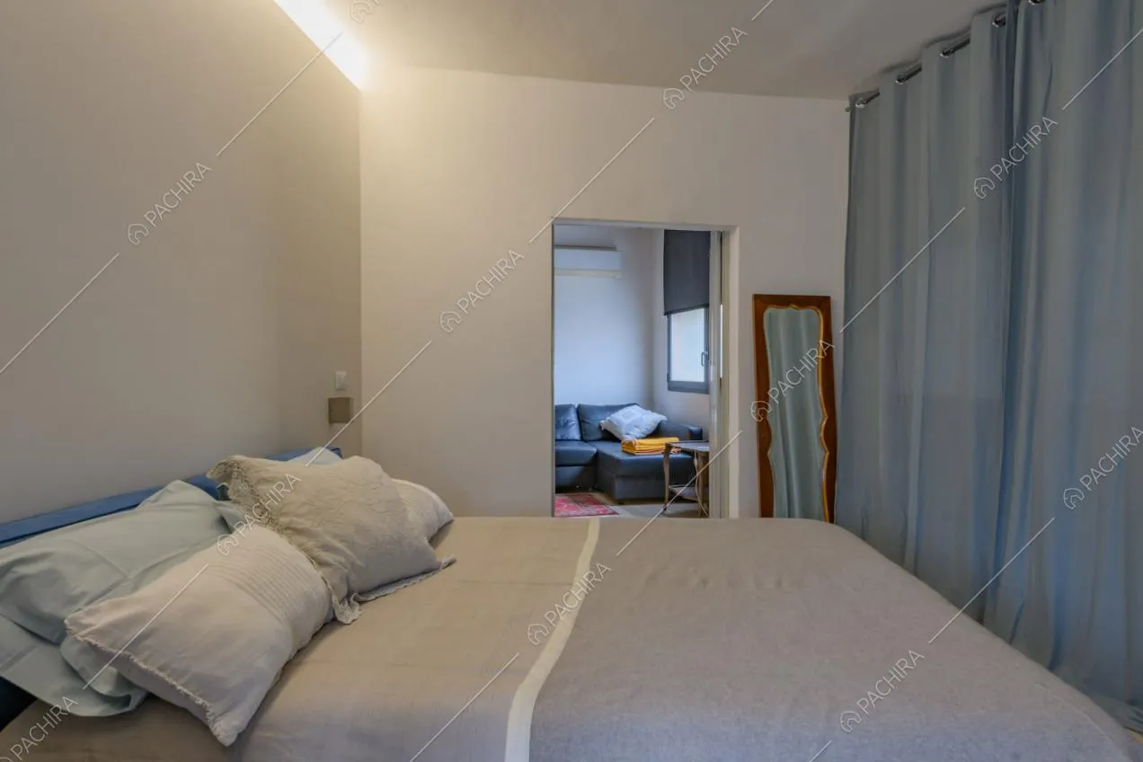 Camera da letto matrimoniale con pareti bianche e vista sul soggiorno con divano angolare