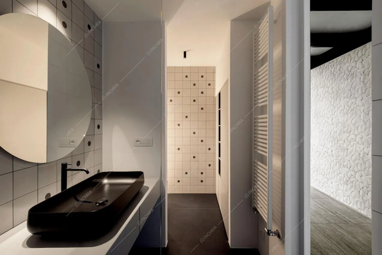 Bagno con pavimento e lavandino nero, pareti con particolari piastrelle e vista sul corridoio