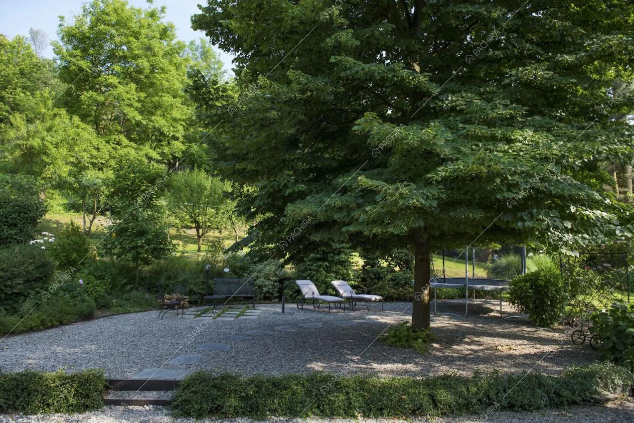 Giardino in ciottoli con sdraio, sedie e una panchina in metallo e trampolino con rete di protezione