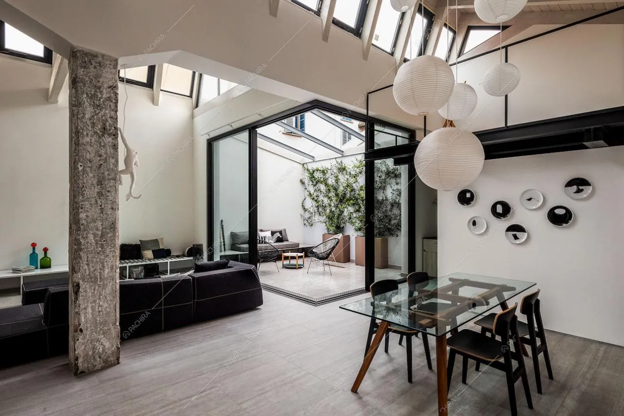 Sala con tavolo da pranzo con piano in vetro, lampadario bianco di design e giardino d'inverno