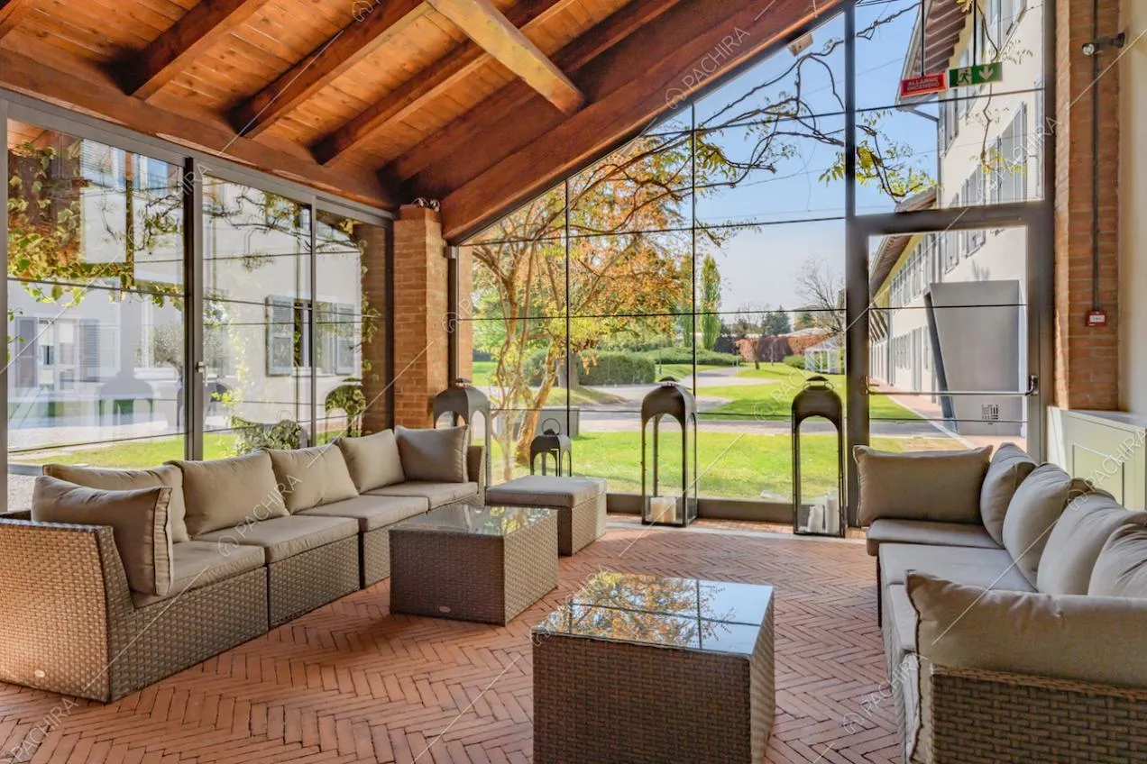 Veranda con soffitto in travi in legno a vista, divanetti e vetrate