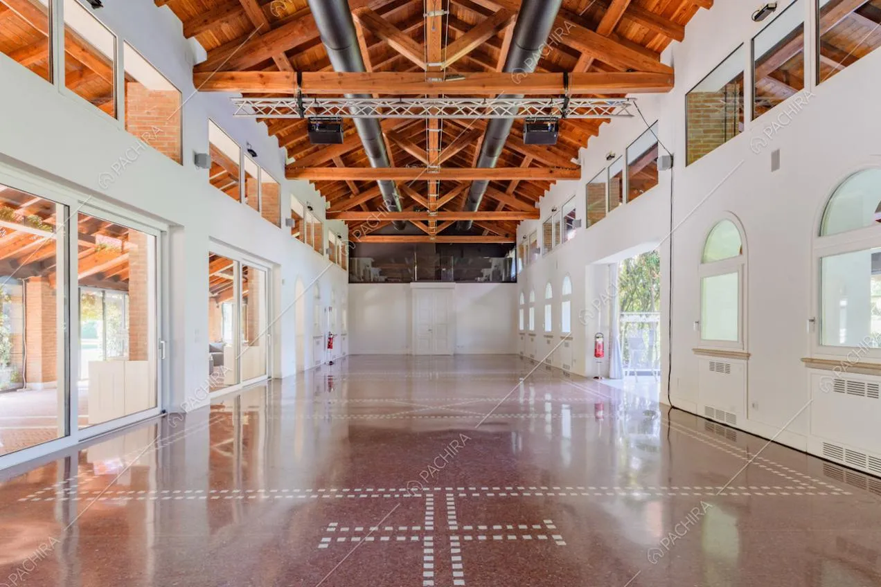 Ampio salone con pareti bianche, porte-finestre e travi in legno a vista
