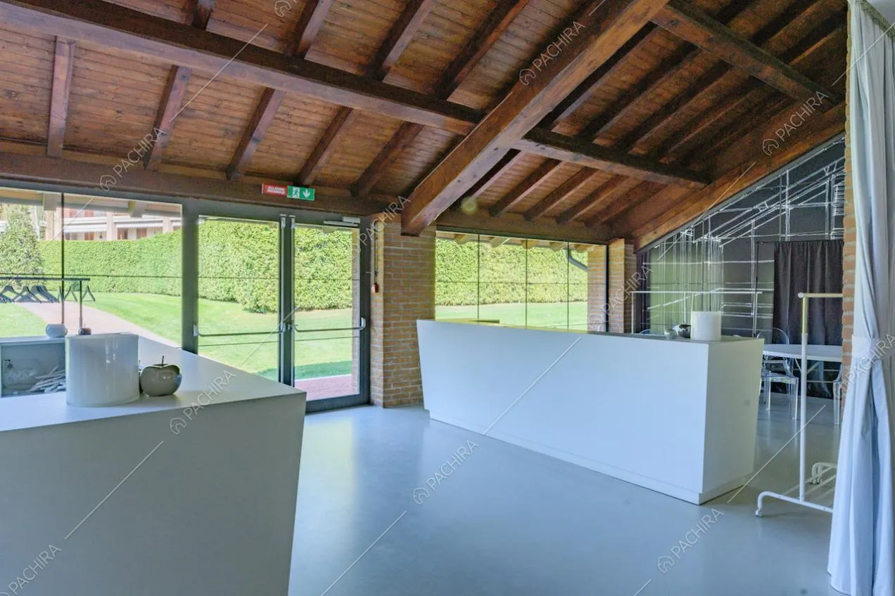 Luminosa veranda con soffitto in travi in legno, tavoli bianchi e colonne