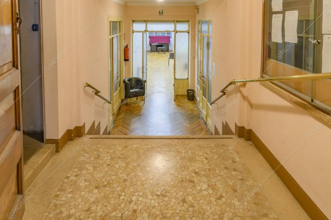 Corridoio dalle pareti rosa con scale per accedere alla sala con pavimento in parquet a spina di pesce, separata da porta e vetri satinata