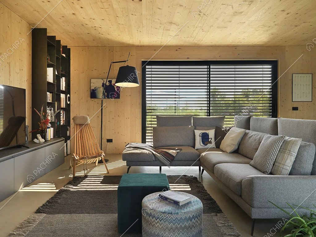 Divano grigio angolare nella zona living con ampie vetrate e legno su pareti e soffitto