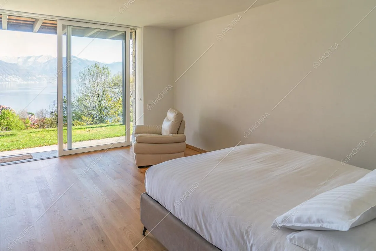 Letto matrimoniale in luminosa camera dalle pareti bianche con porta-finestra scorrevole