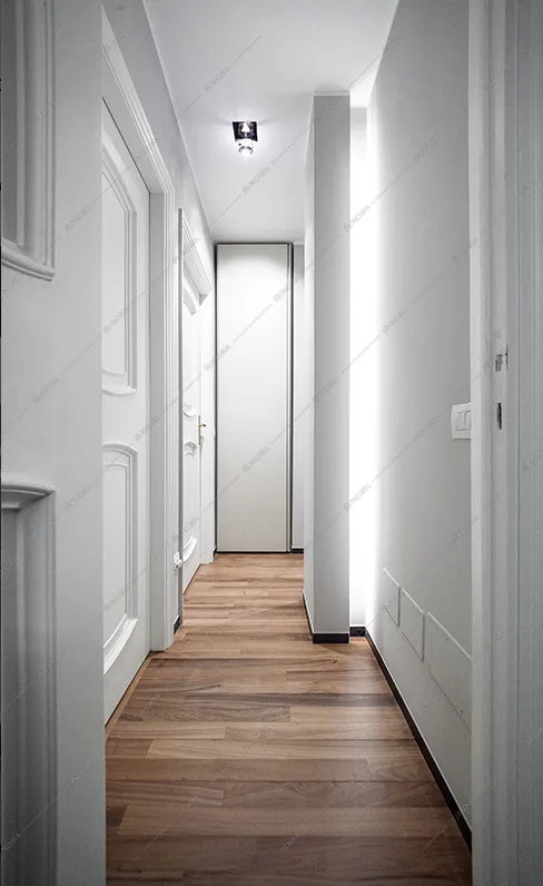 Corridoio con pareti cassettonate bianche e pavimento in parquet