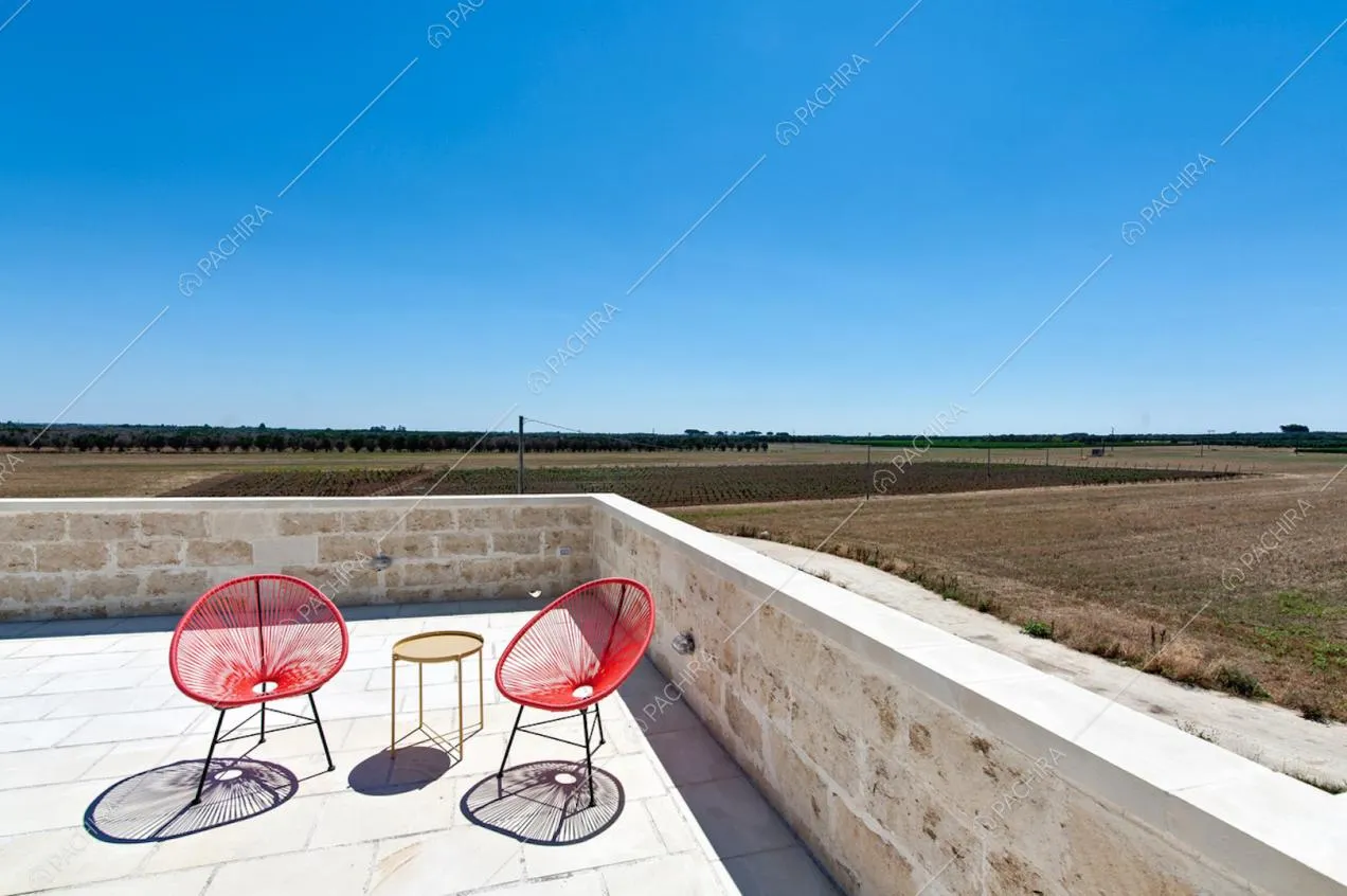 Muretto in pietra, sedie tonde rosse da esterni e vista sulla campagna 