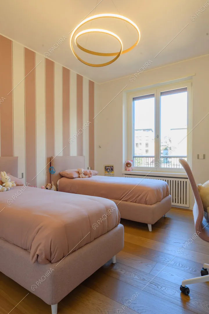 Camera da letto dei bambini con letti singoli rosa e carta da parati a colonne bianche e rosa