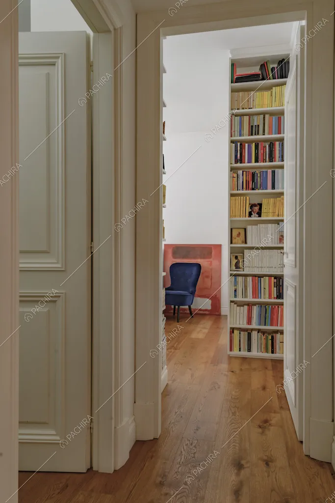 Corridoio dal pavimento in parquet, libreria e porta bianca in legno con boiserie
