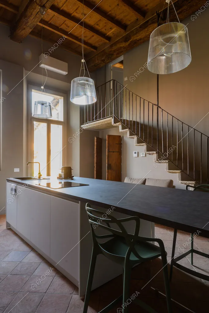 Isola della cucina con fornelli a induzione, sedie e soffitto in travi in legno a vista