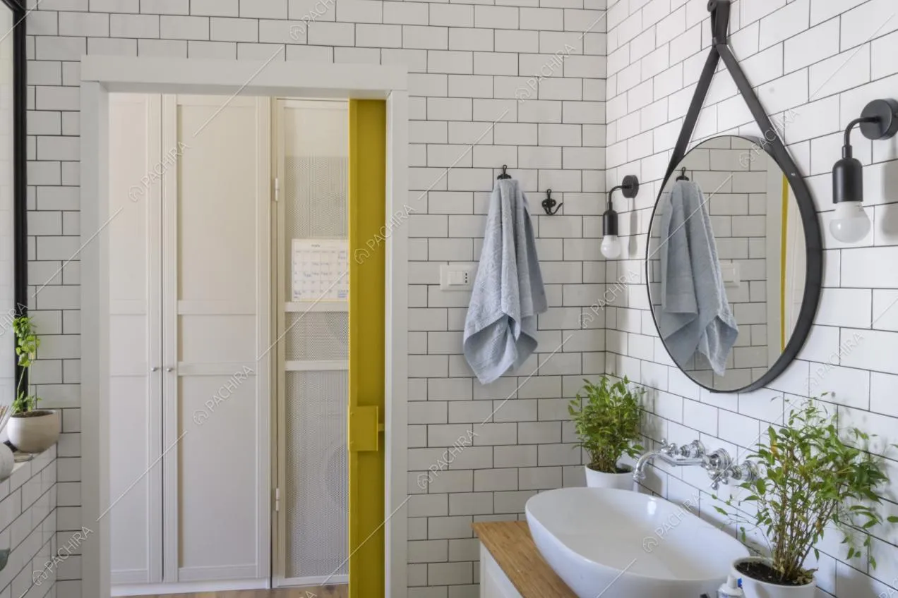 Specchio tondo appeso sulla parete del bagno rivestite di piastrelle bianche