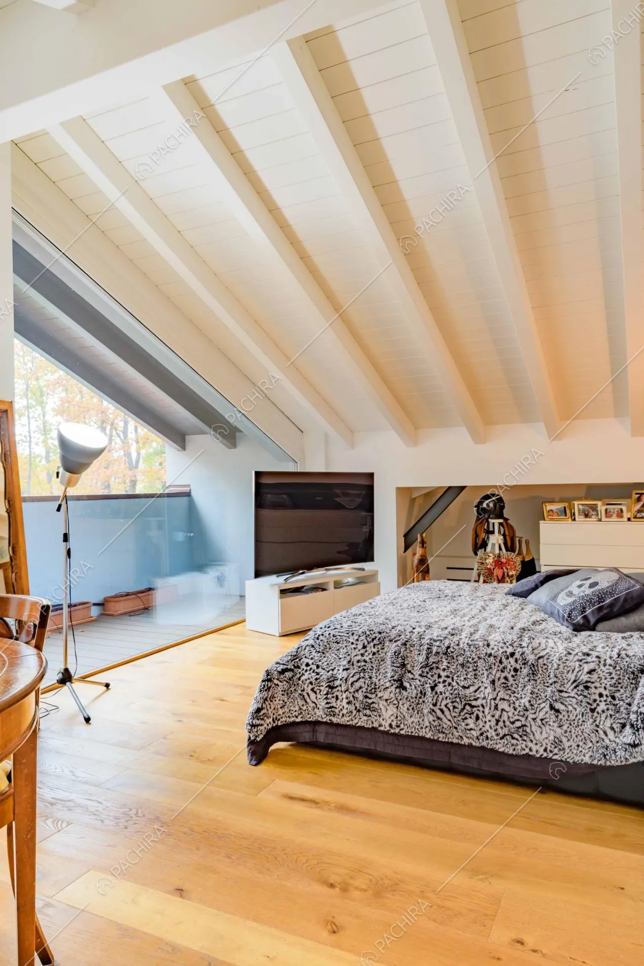 Camera da letto matrimoniale con pavimento in parquet, soffitto in legno bianco con travi a vista e balcone privato