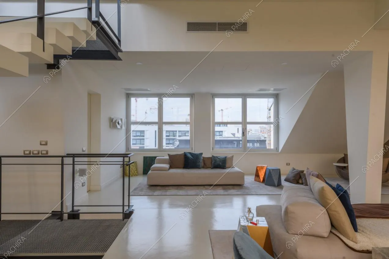 Divani nella zona living con pavimento in resina bianco, scale in metallo e finestre in stile industriale