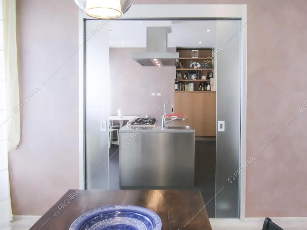 Porta doppia in vetro aperta, vista sull'isola della cucina dal tavolo da pranzo