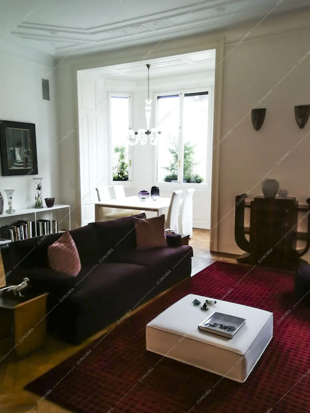Salotto con divano viola, pareti bianche, boiserie sul soffitto e vista sul tavolo da pranzo