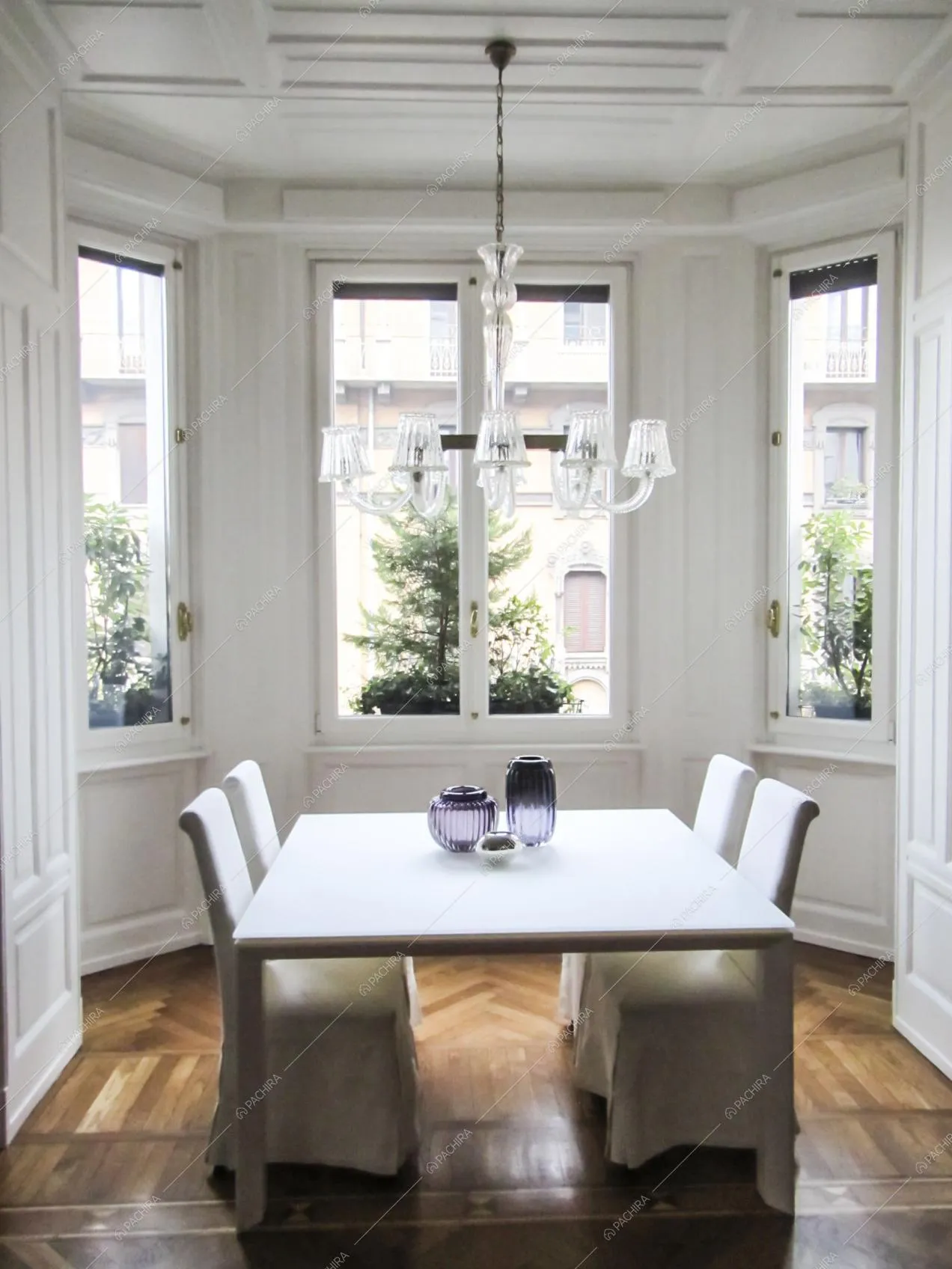 Tavolo da pranzo bianco nella luminosa sala con boiserie alle pareti e al soffito, lampadario classico