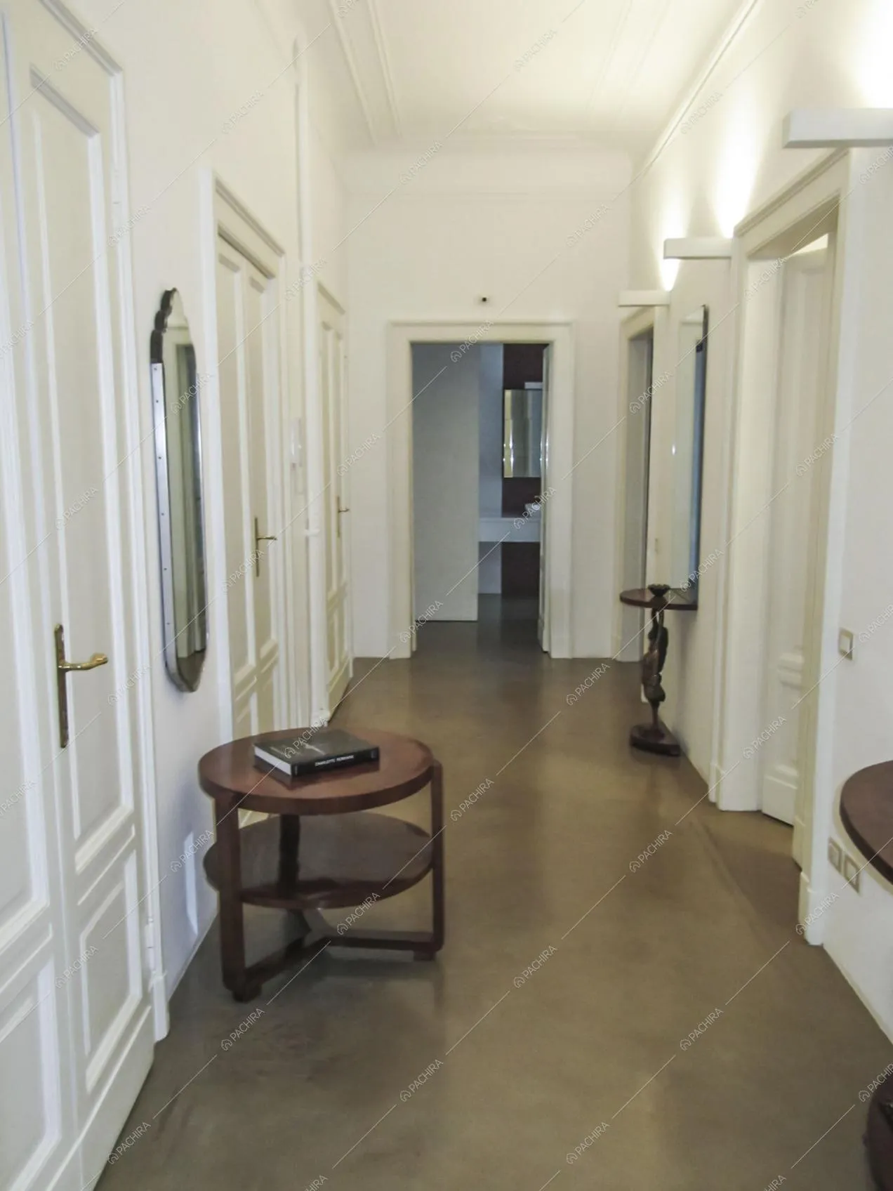 Pavimento in resina con antichi tavolini in legno nel corridoio bianco con boiserie sul soffitto