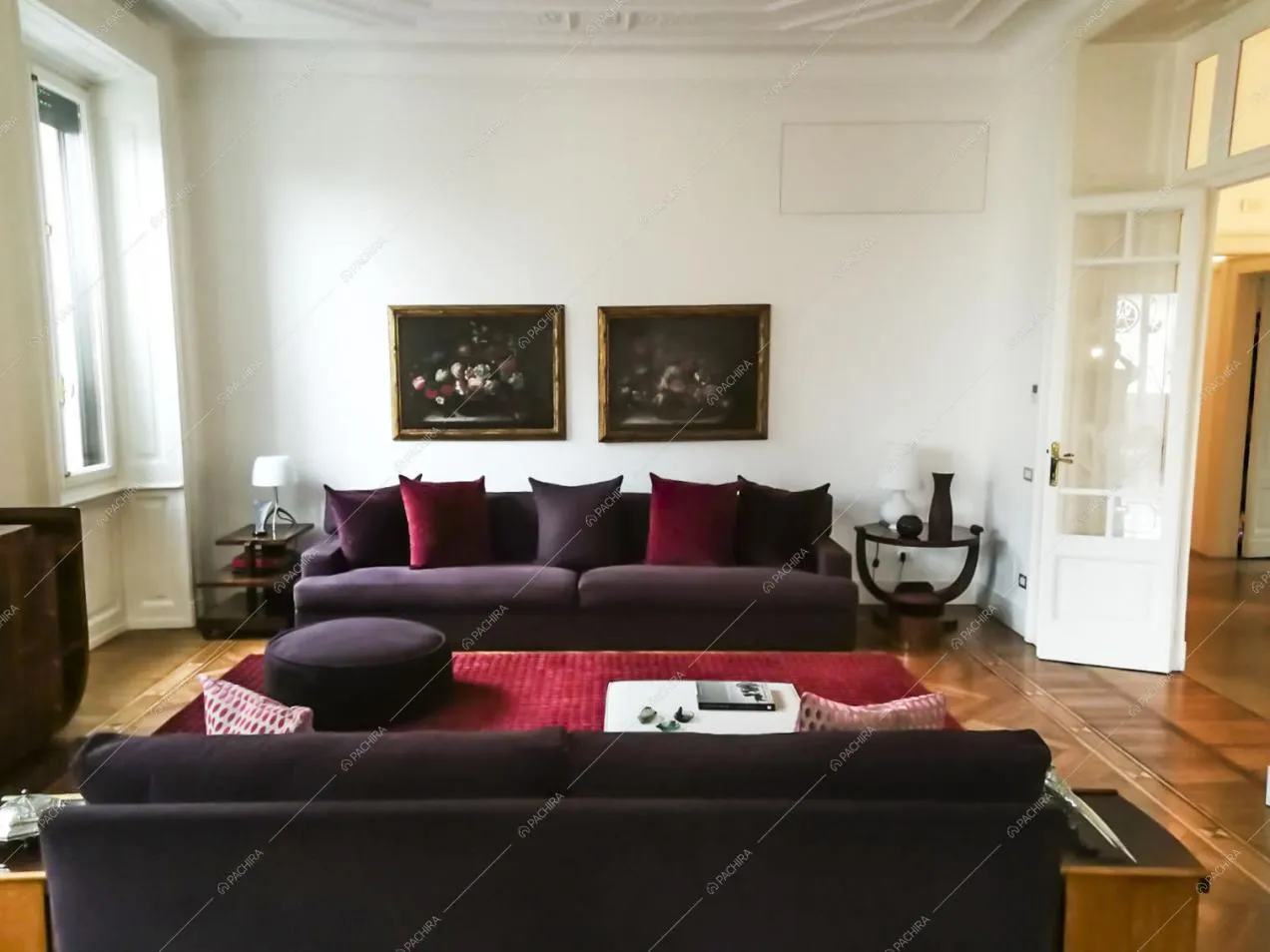 Salotto con divani viola, pareti bianche, boiserie sul soffitto, pavimento in parquet a spina di pesce e porta a vetri