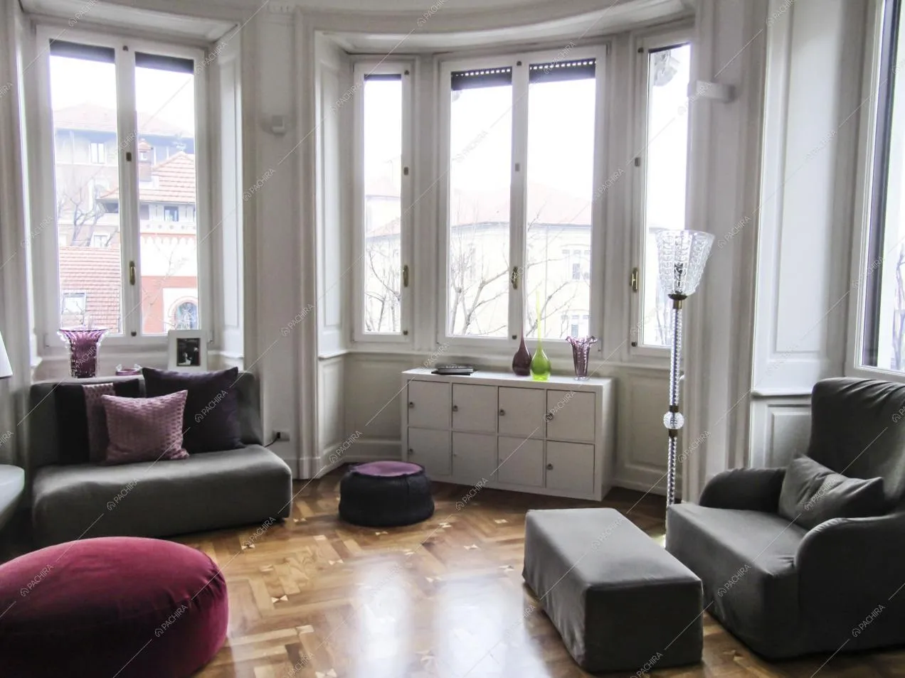 Soggiorno con divani e pouf, pavimento in parquet e ampie finestre che illuminano l'ambiente
