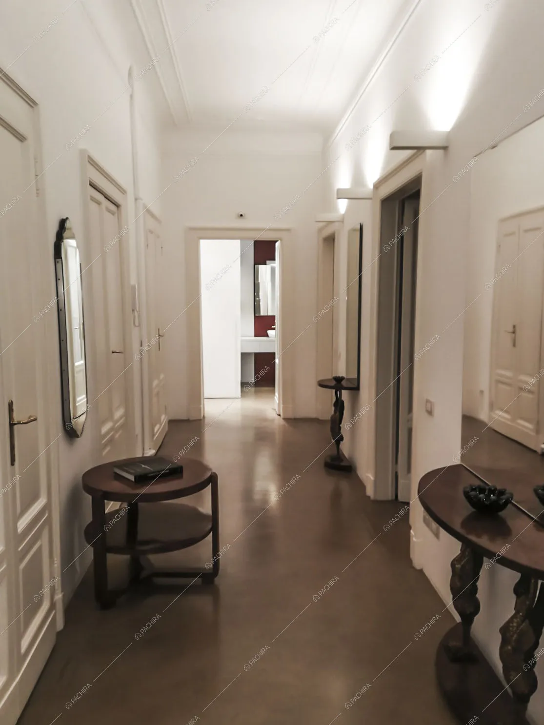 Corridoio con antichi tavolini in legno e soffitto e pareti bianchi con boiserie