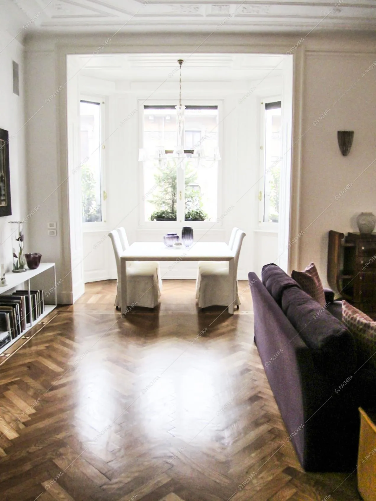 Sala con pavimento in parquet a spina di pesce, divano viola e tavolo da pranzo bianco