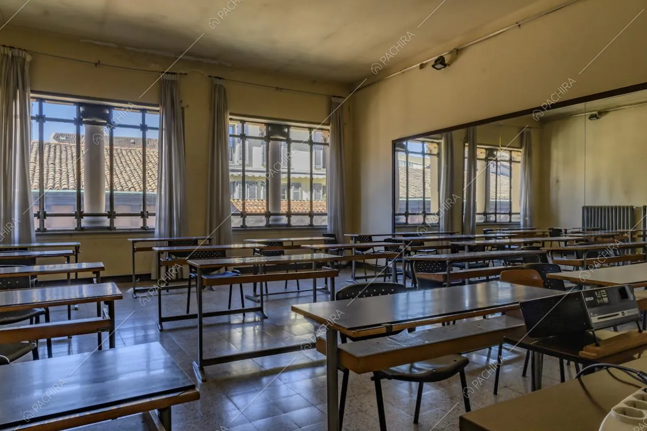 Ampia aula dalle pareti gialle, con specchio a parete, numerosi banchi e pavimento in piastrelle