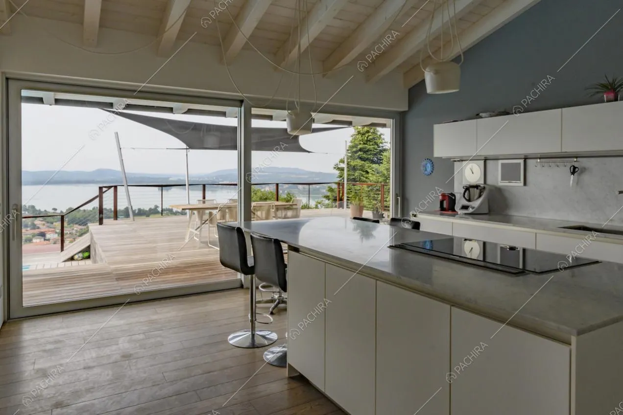 Isola della cucina con piano in marmo, fornelli a induzione, sgabelli e vista sul lago attraverso le vetrate