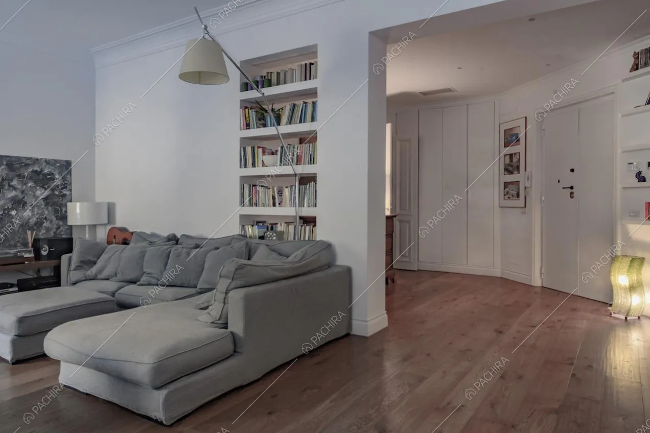 Vista sul divano grigio e sull'ingresso con pareti e soffitto bianchi con boiserie