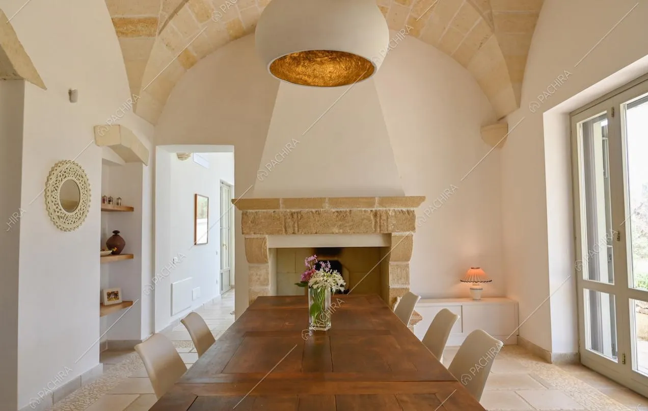 Ampia sala da pranzo dalle pareti bianche con tavolo in legno, camino e pavimento in pietra