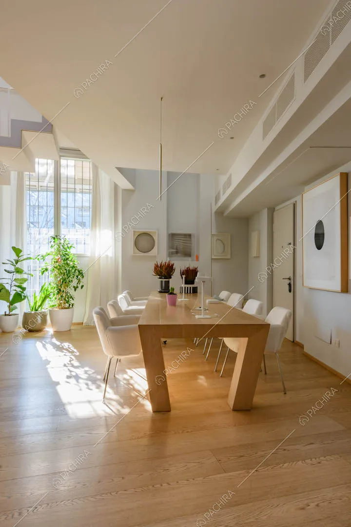 Tavolo da pranzo in legno con sedie bianche nella spaziosa sala con pavimento in parquet