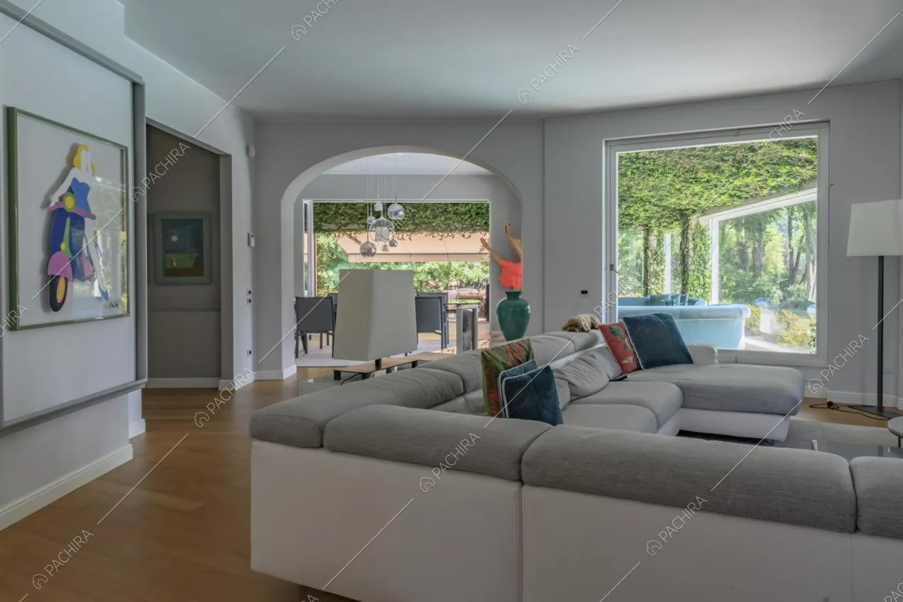 Divano angolare grigio e bianco nel salotto con pavimento in parquet e vista tramite l'arco a volta sulla sala da pranzo